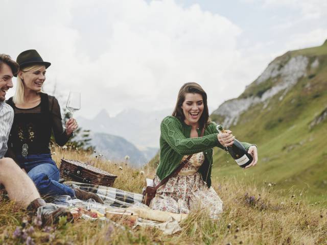 Freunde öffnen eine Sektflasche in den Alpen beim Picknick